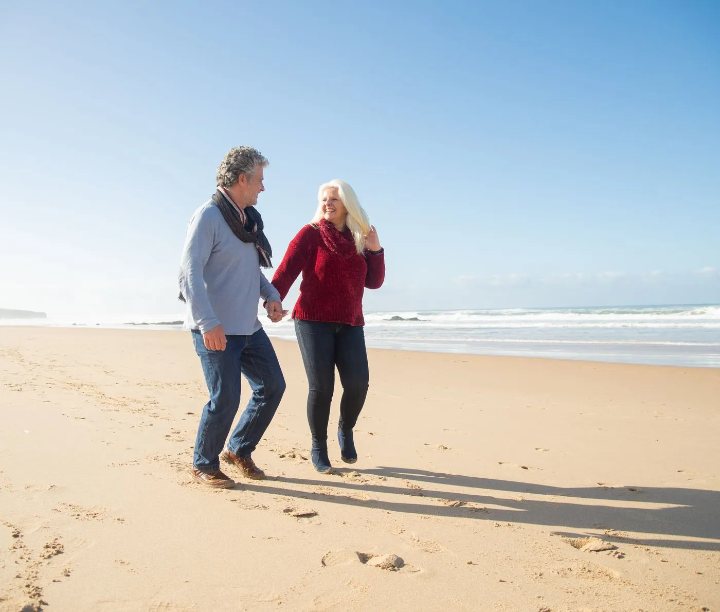 A retired couple laughing together on a sunny beach walk